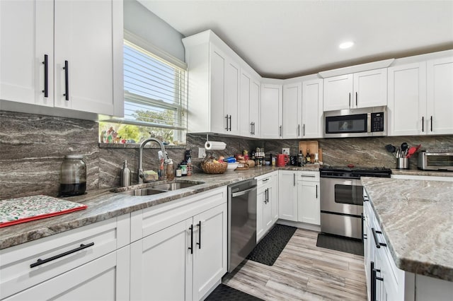 kitchen featuring light stone countertops, a sink, stainless steel appliances, white cabinets, and backsplash