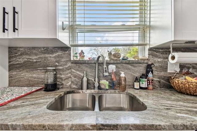 kitchen with backsplash, white cabinets, light stone countertops, and a sink