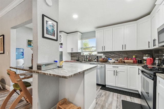 kitchen featuring backsplash, light wood-style floors, white cabinets, stainless steel appliances, and a sink