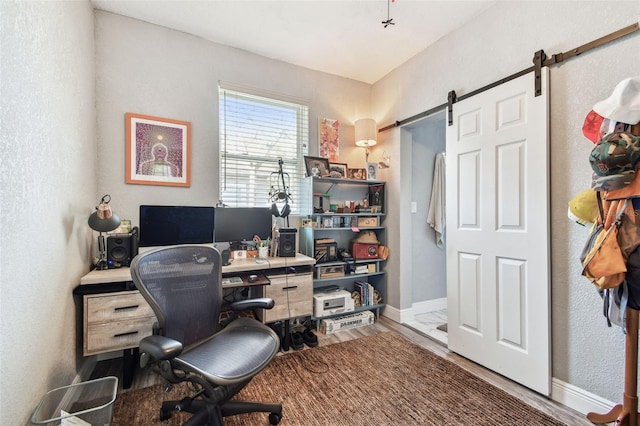 office area with a barn door, wood finished floors, and baseboards