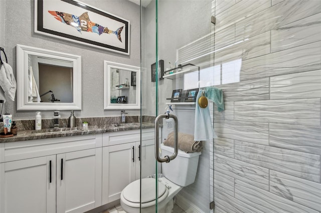 bathroom with vanity, toilet, a textured wall, and tiled shower