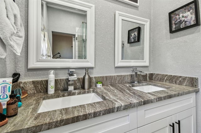 bathroom with double vanity, an enclosed shower, a textured wall, and a sink