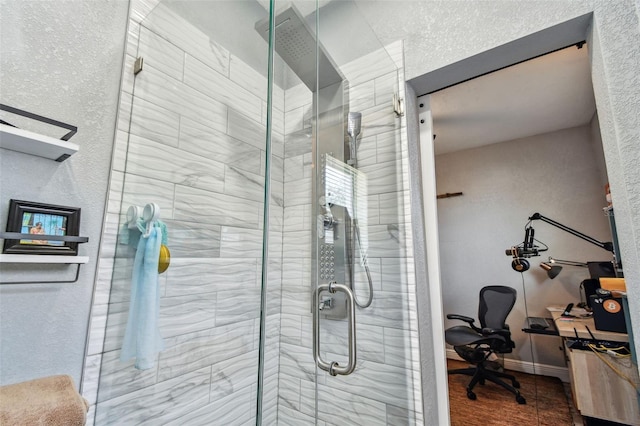 bathroom with a textured wall, a stall shower, and baseboards