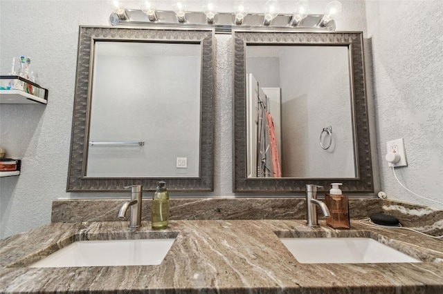 full bath with a sink, double vanity, and a textured wall