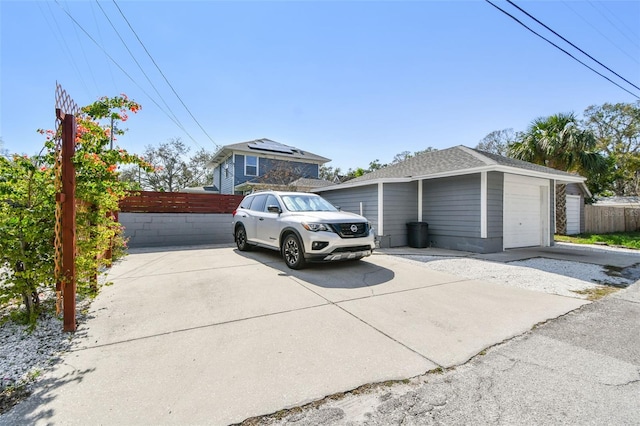 view of property exterior with an outdoor structure, roof with shingles, concrete driveway, and fence