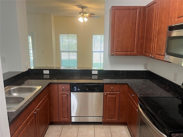 kitchen with dark stone counters, appliances with stainless steel finishes, a peninsula, a sink, and light tile patterned flooring