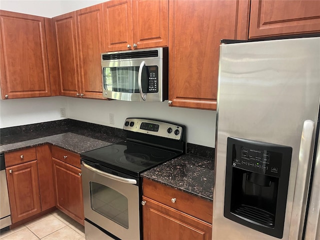 kitchen with stainless steel appliances, dark stone counters, brown cabinets, and light tile patterned flooring