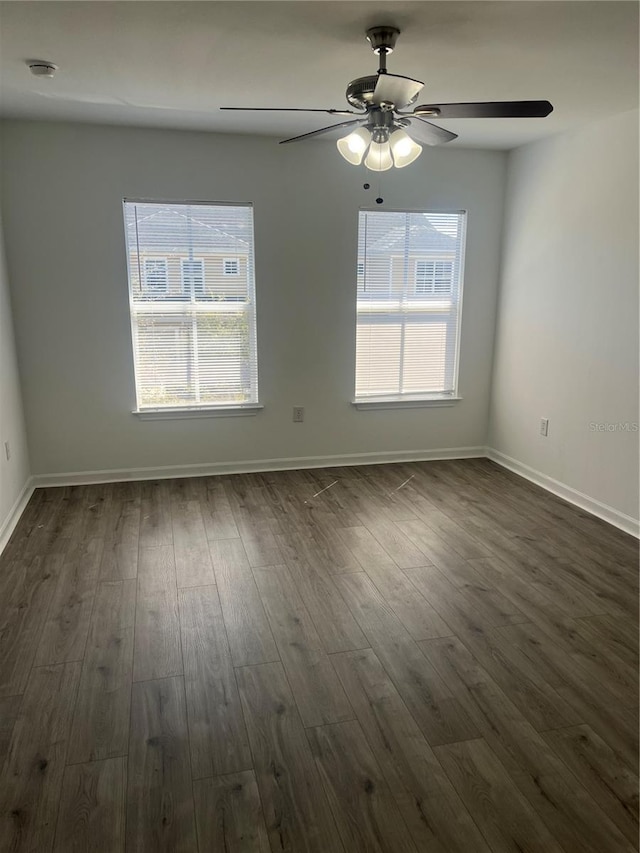 empty room featuring dark wood-style floors, a healthy amount of sunlight, and baseboards