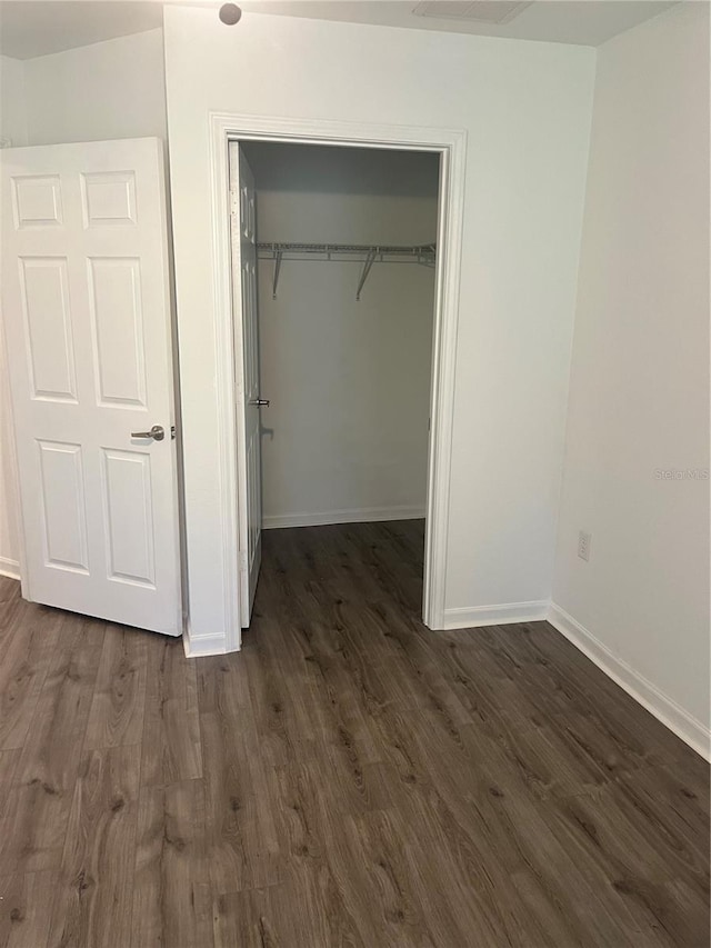 unfurnished bedroom featuring dark wood-style floors, a closet, a walk in closet, and baseboards