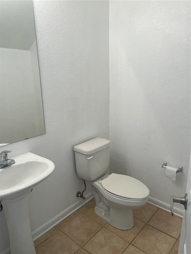 half bathroom with baseboards, a sink, toilet, and tile patterned floors