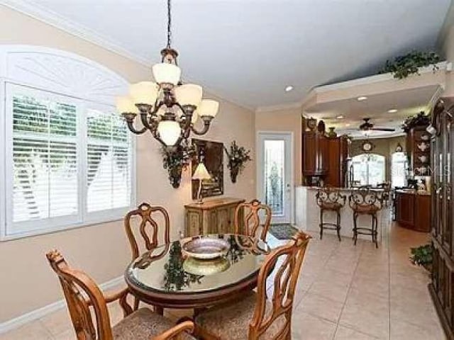 dining space with light tile patterned floors, ceiling fan with notable chandelier, baseboards, and crown molding