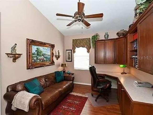 home office featuring a ceiling fan, vaulted ceiling, built in desk, and wood finished floors