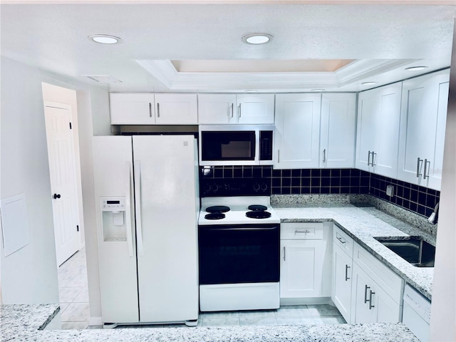 kitchen with a tray ceiling, decorative backsplash, white cabinets, white appliances, and a sink