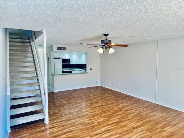 unfurnished living room featuring light wood-type flooring, visible vents, a ceiling fan, a textured ceiling, and stairway