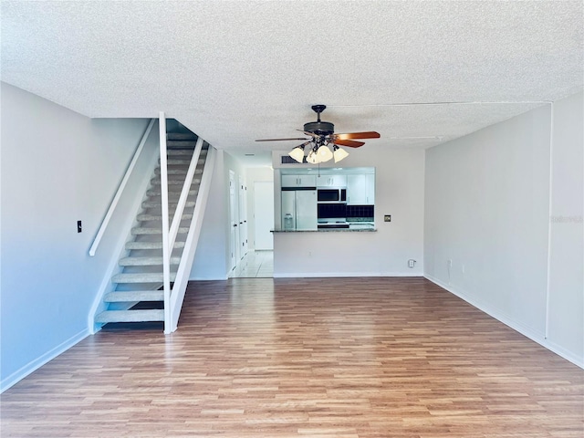 unfurnished living room featuring a textured ceiling, stairway, light wood-type flooring, and ceiling fan