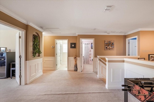 hall with visible vents, light carpet, an upstairs landing, ornamental molding, and attic access