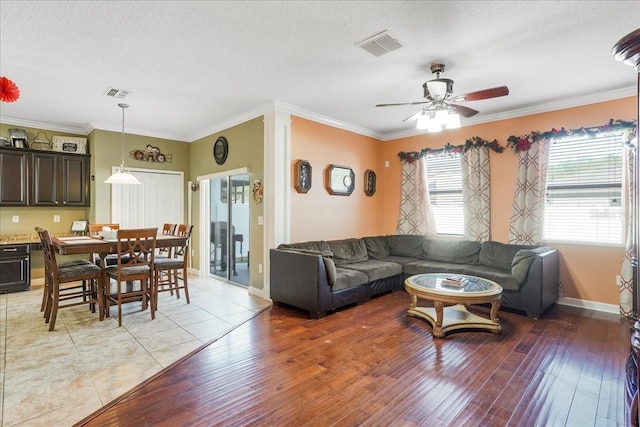 living area featuring visible vents, ceiling fan, a textured ceiling, crown molding, and light wood-type flooring