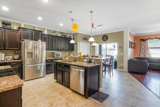kitchen featuring a kitchen island with sink, ornamental molding, a sink, stainless steel appliances, and light tile patterned flooring