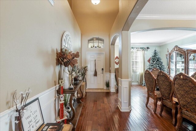 foyer entrance with crown molding, arched walkways, dark wood-style flooring, and wainscoting