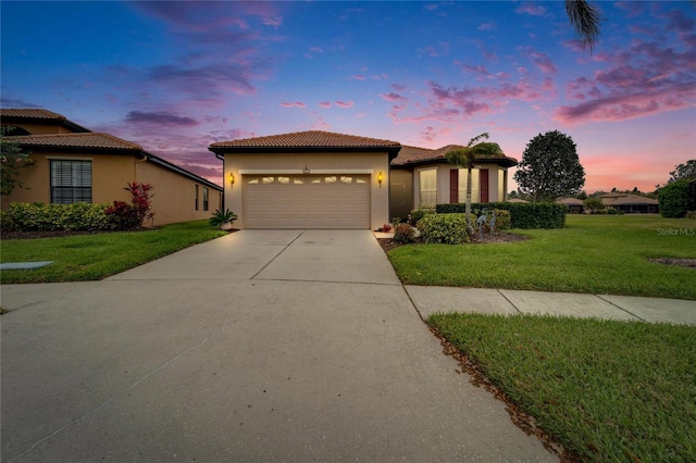 mediterranean / spanish-style home with stucco siding, driveway, a tile roof, a yard, and an attached garage