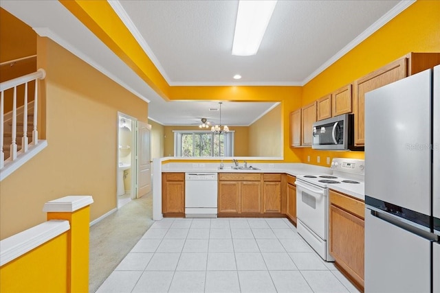 kitchen with a peninsula, white appliances, a sink, light countertops, and crown molding