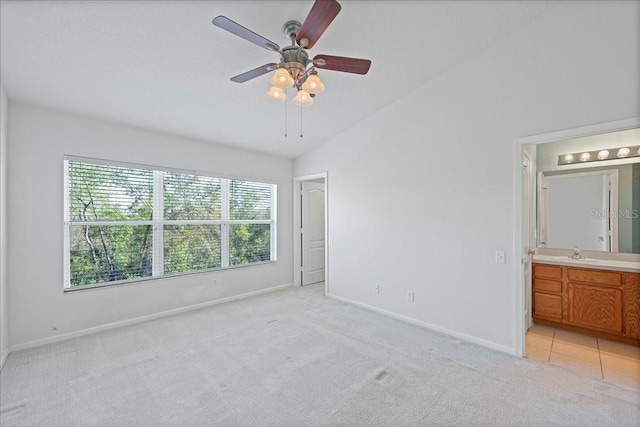 unfurnished bedroom featuring lofted ceiling, connected bathroom, light carpet, a sink, and baseboards