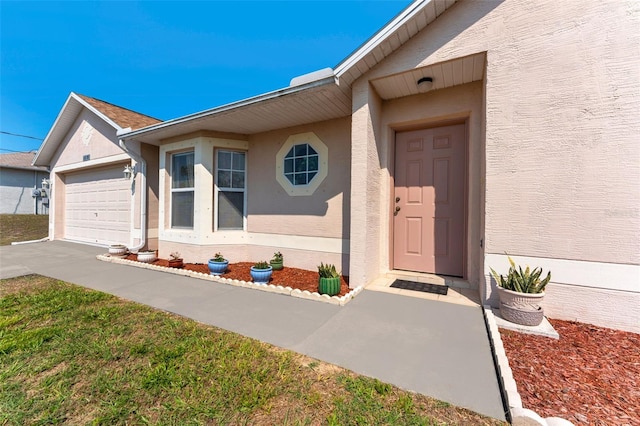 view of exterior entry featuring stucco siding, driveway, and a garage