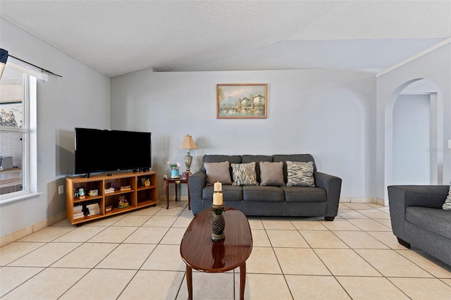 living area featuring baseboards, light tile patterned flooring, arched walkways, vaulted ceiling, and a textured ceiling