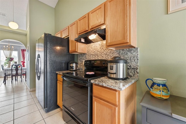 kitchen with tasteful backsplash, under cabinet range hood, light tile patterned flooring, arched walkways, and black appliances