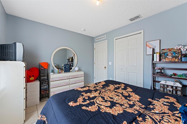 bedroom featuring tile patterned flooring, visible vents, a closet, and a textured ceiling