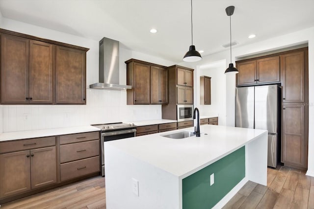 kitchen with wall chimney range hood, light wood-style floors, appliances with stainless steel finishes, and a sink