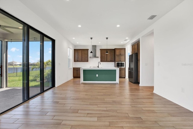 kitchen featuring stainless steel microwave, light countertops, light wood-style flooring, freestanding refrigerator, and wall chimney exhaust hood