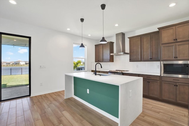 kitchen featuring a sink, stainless steel microwave, a wealth of natural light, and wall chimney range hood