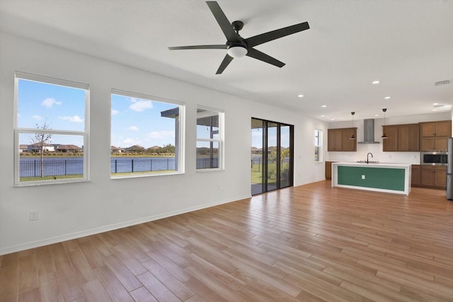 unfurnished living room with baseboards, light wood-style flooring, recessed lighting, a sink, and a water view