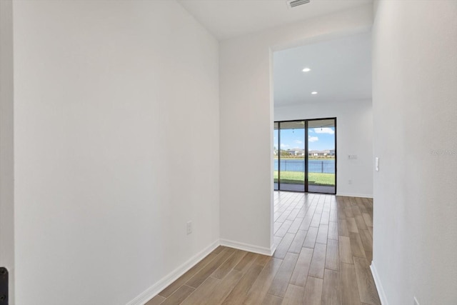 hall with visible vents, baseboards, light wood finished floors, recessed lighting, and a water view