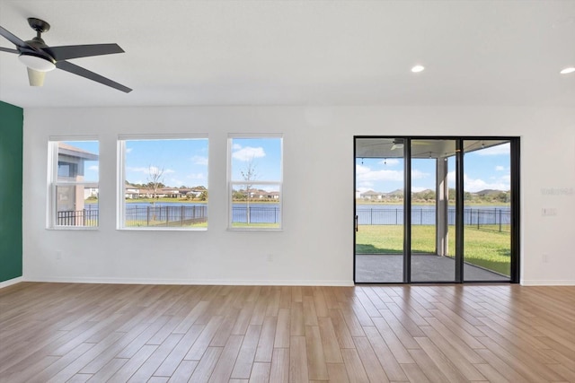 unfurnished room with a ceiling fan, baseboards, light wood-style flooring, recessed lighting, and a water view