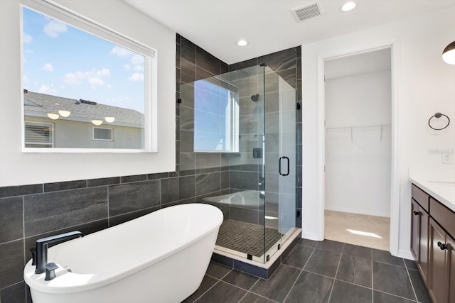 full bath featuring visible vents, a walk in closet, a freestanding bath, a stall shower, and vanity