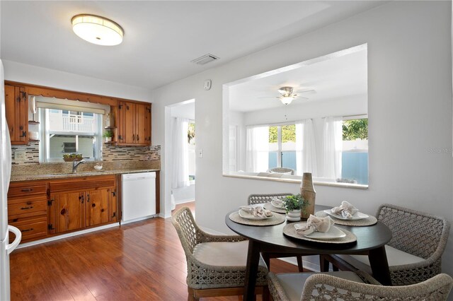 kitchen with white dishwasher, a sink, visible vents, brown cabinets, and tasteful backsplash