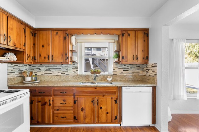 kitchen with brown cabinetry, white appliances, a sink, and backsplash