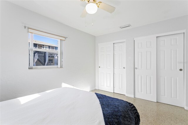 bedroom with a ceiling fan, speckled floor, and two closets