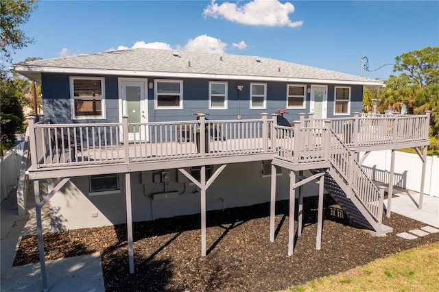 rear view of house with a deck, a shingled roof, stairway, and fence