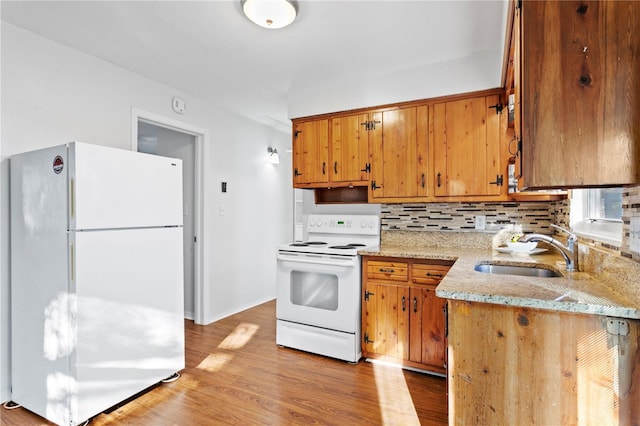 kitchen featuring white appliances, a sink, light wood-style floors, decorative backsplash, and brown cabinets