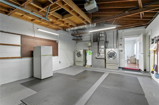 garage featuring concrete block wall, freestanding refrigerator, and washer and dryer