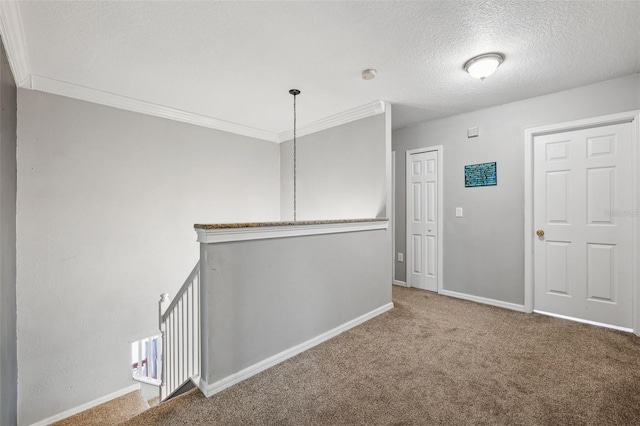 carpeted spare room featuring a textured ceiling, ornamental molding, and baseboards