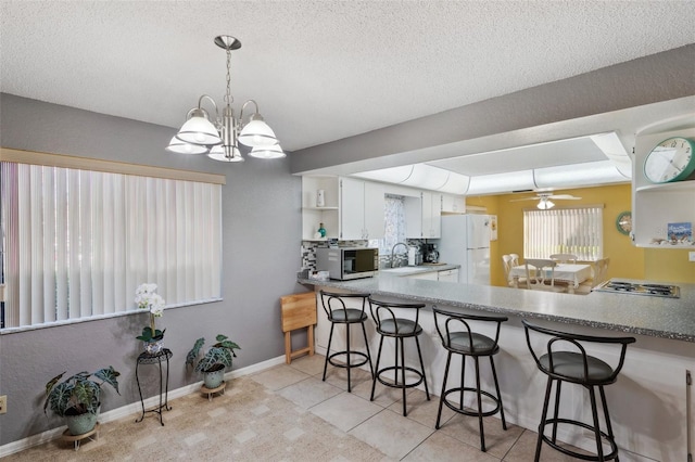 kitchen with stainless steel microwave, freestanding refrigerator, stovetop, white cabinetry, and open shelves