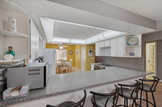 kitchen with a breakfast bar, a sink, a ceiling fan, white cabinets, and open shelves