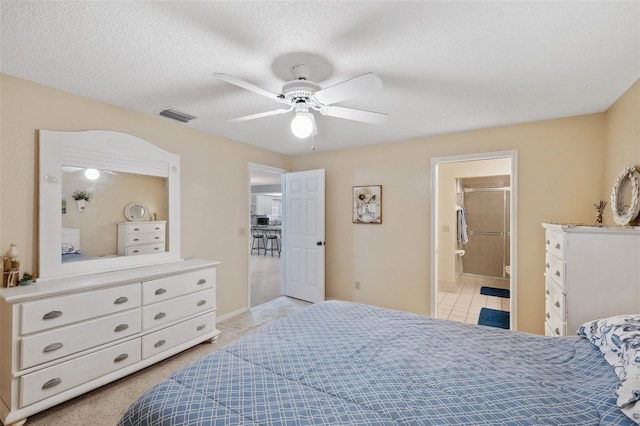 bedroom featuring light carpet, visible vents, a ceiling fan, ensuite bath, and a textured ceiling