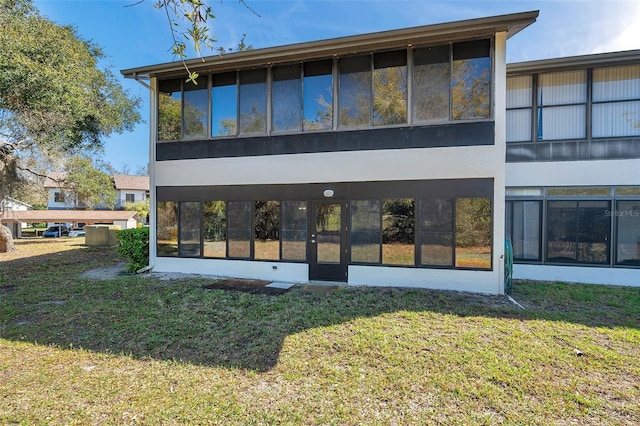 rear view of house with a sunroom, a lawn, and stucco siding