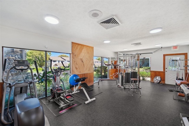 workout area with wooden walls, visible vents, a textured ceiling, and wainscoting