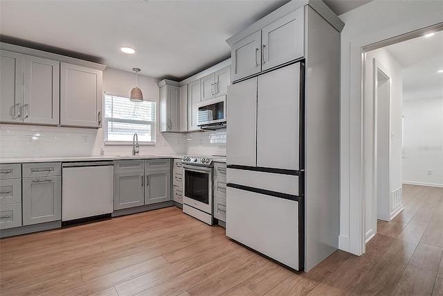 kitchen featuring appliances with stainless steel finishes, light wood-type flooring, a sink, and gray cabinetry